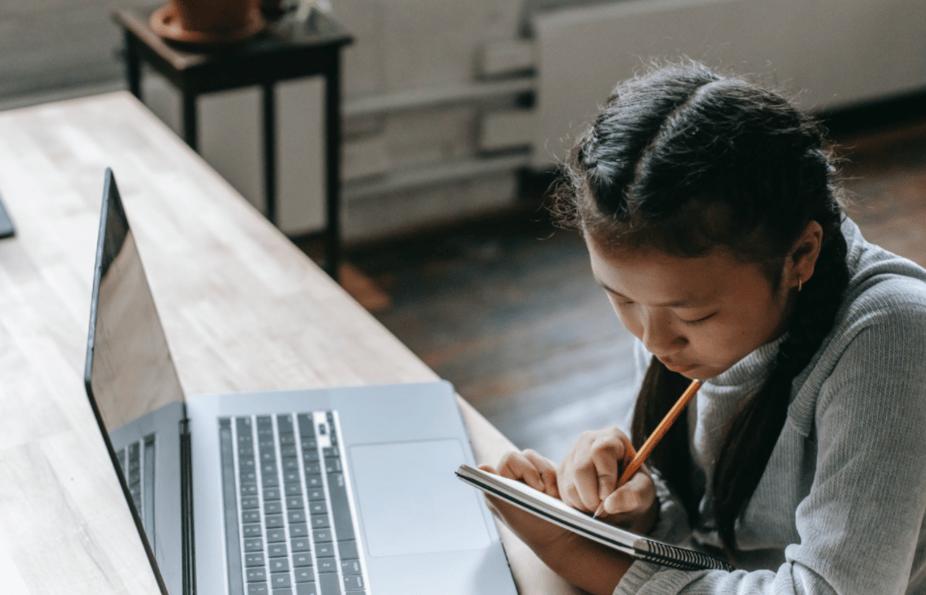 Girl with braids sits in front of a laptop making notes in a notebook
